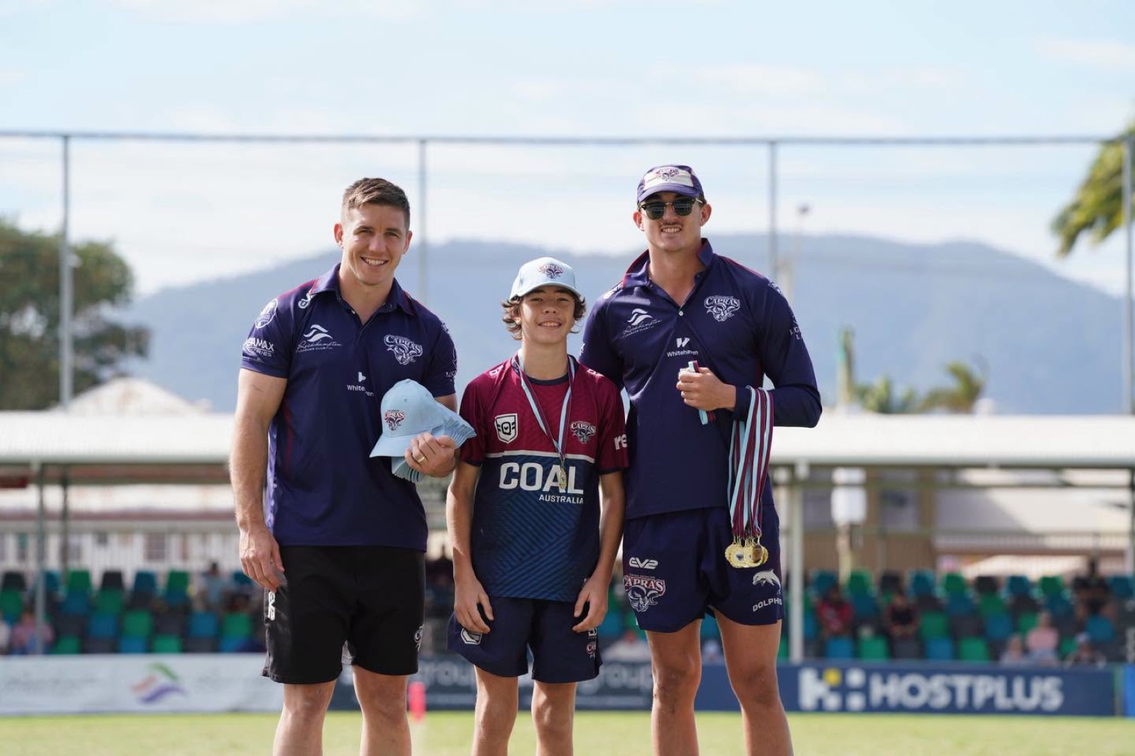 Two Capras players with a junior player wearing his medals after a game